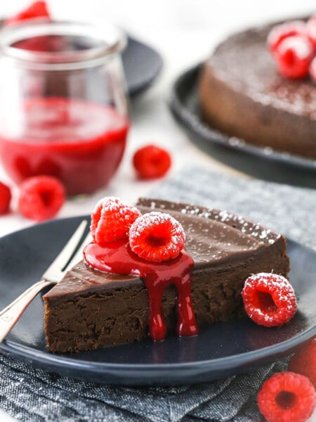 A serving of gluten-free chocolate cake on a plate with raspberry sauce and fresh raspberries on top of it