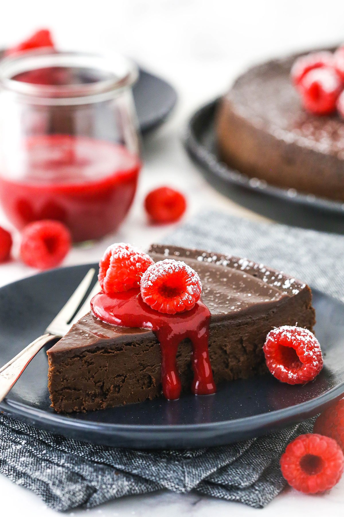 A serving of gluten-free chocolate cake on a plate with raspberry sauce and fresh raspberries on top of it