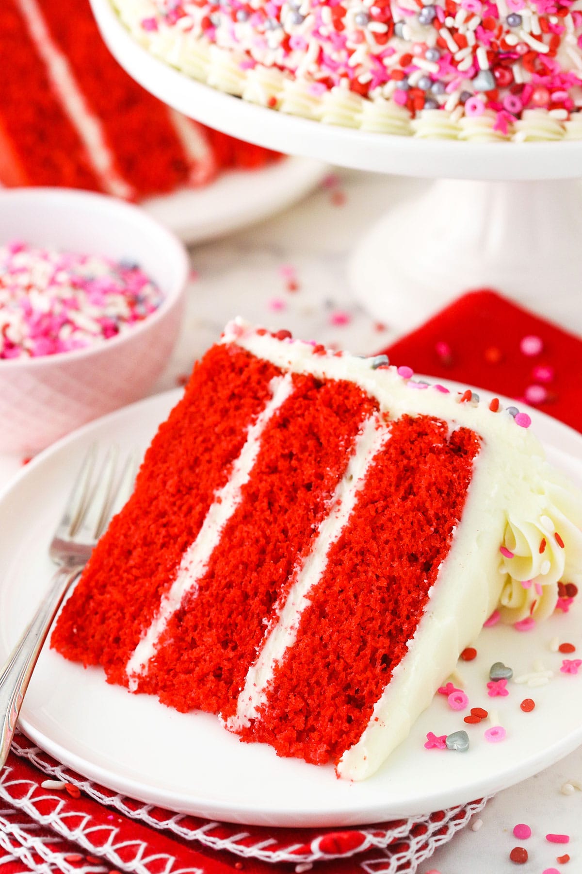 A piece of red velvet layer cake on a plate with a metal dessert fork