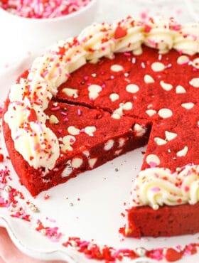 A cookie cake on a serving dish with one slice removed from the plate and a second slice cut off of the cake