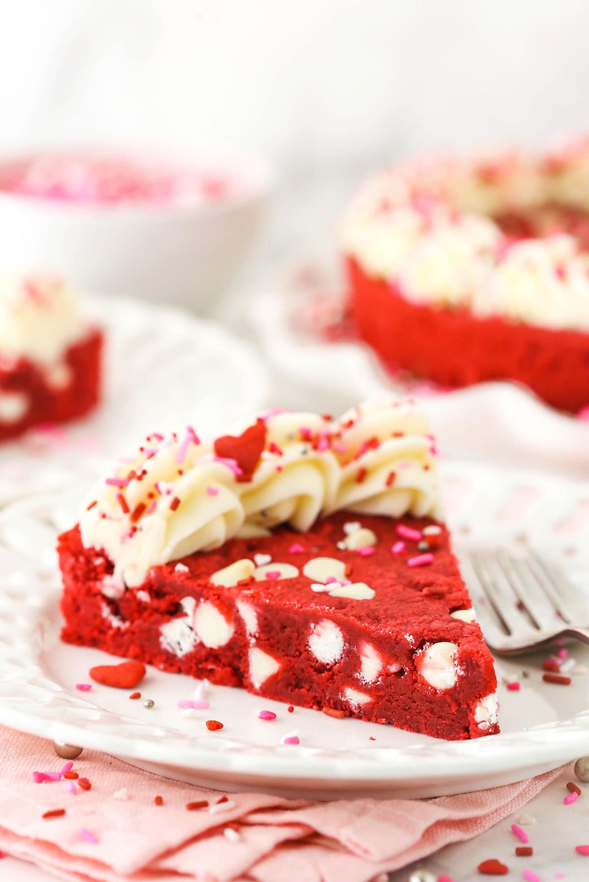 A piece of cookie cake on a plate with a fork and the remaining cake in the background