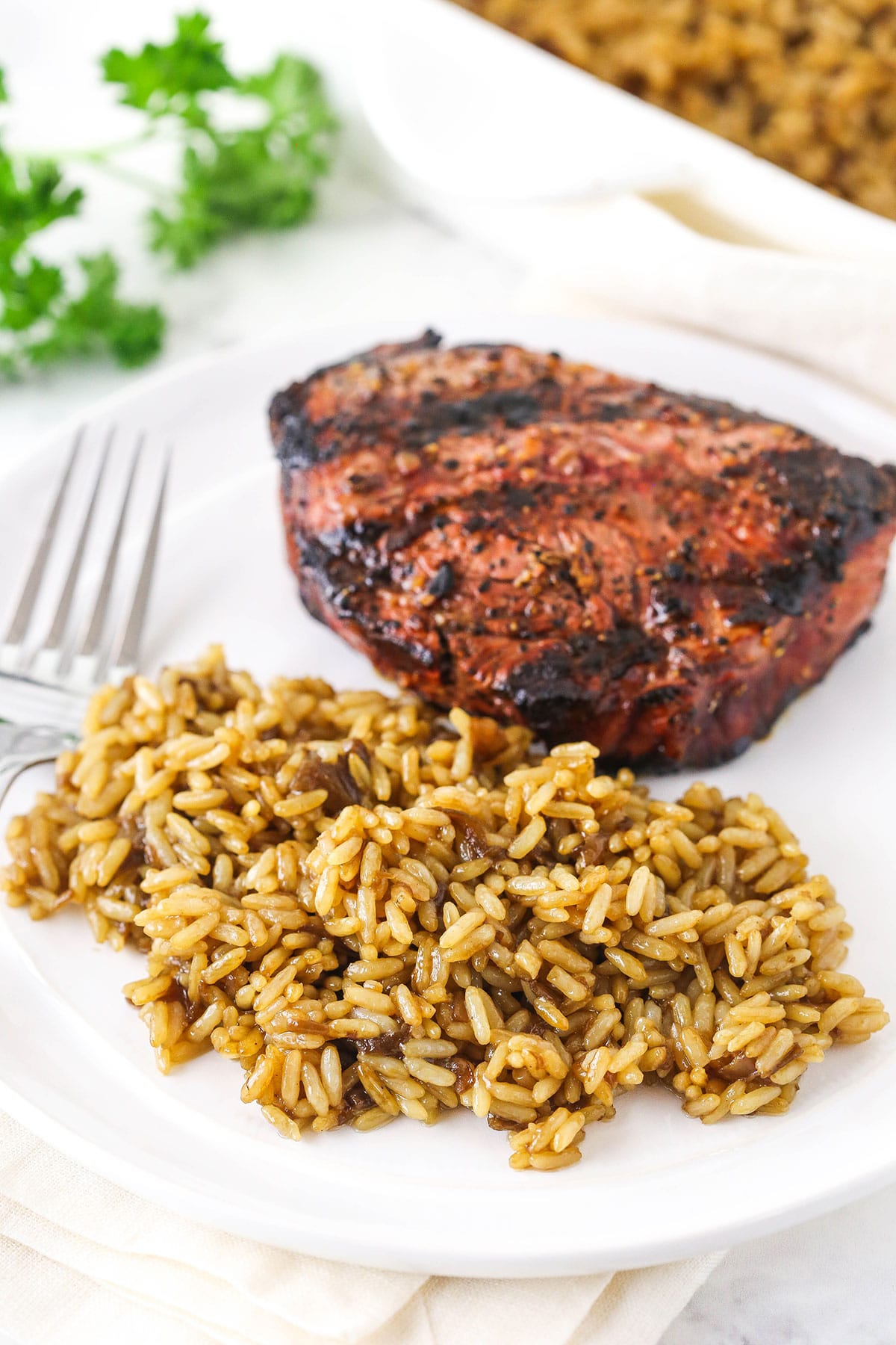 A serving of butter rice beside a piece of medium-well meat on a dinner plate