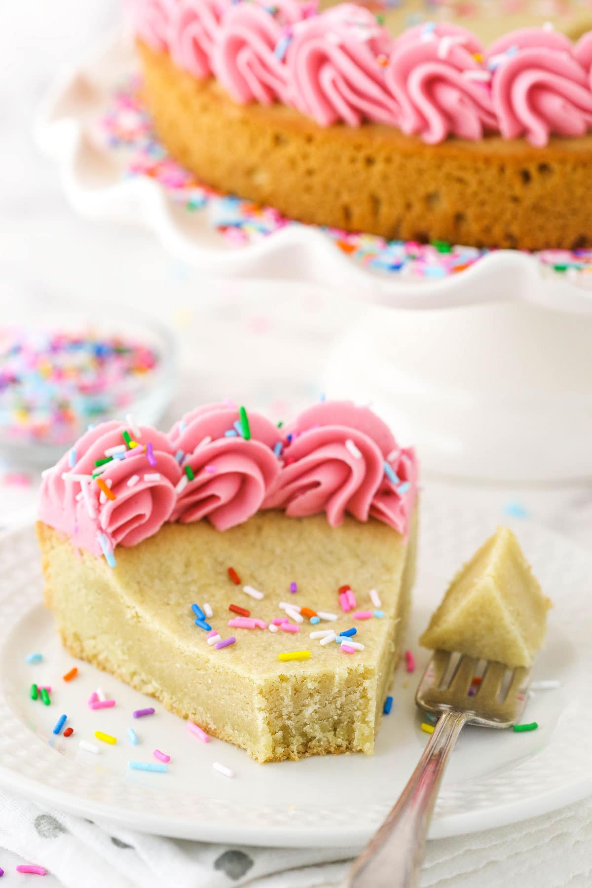 A small slice of cake on a white plate. A bite-sized piece is on the fork, lying on the plate next to the slice.