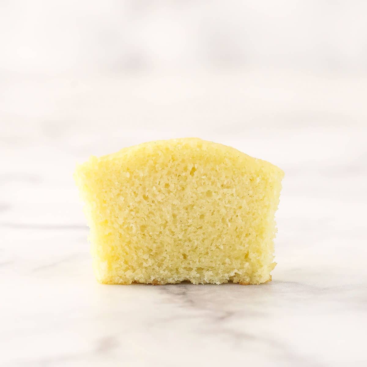 An easy homemade vanilla cupcake on a countertop that has been cut in half with a knife