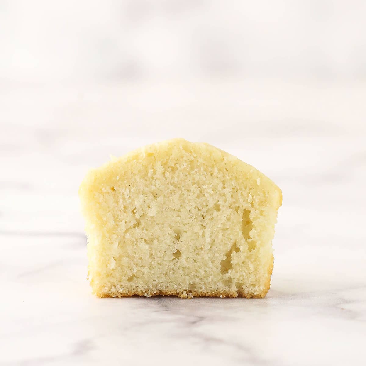 A close-up shot of half of a fluffy vanilla cupcake on top of a marble counter