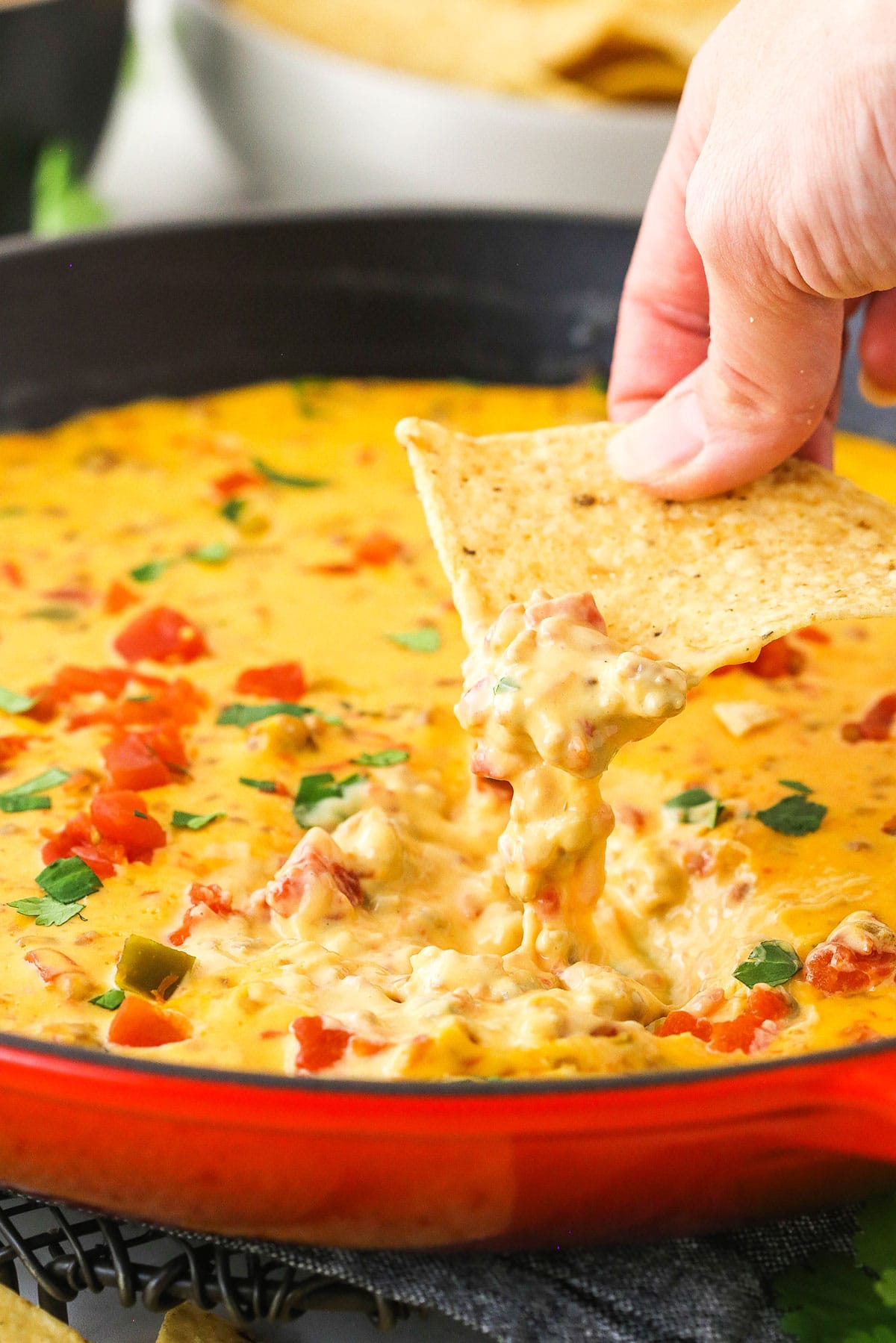 A woman's hand is dipping a tortilla chip into a skillet of cheese dip.