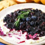 A plate full of appetizer dip with some missing and bread & crackers behind it