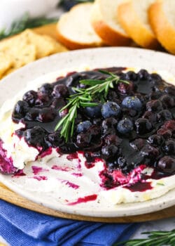 A plate full of appetizer dip with some missing and bread & crackers behind it