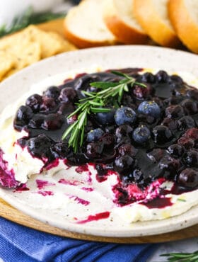 A plate full of appetizer dip with some missing and bread & crackers behind it