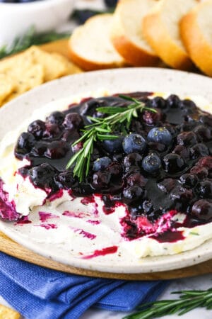 A plate full of appetizer dip with some missing and bread & crackers behind it