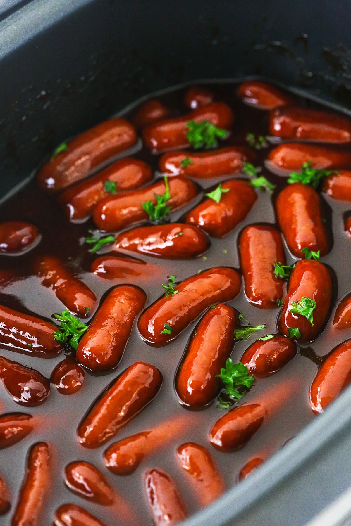 Little smokies sausages in a Crockpot with the sauce mixture and fresh chopped parsley