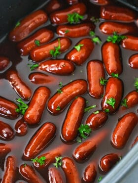 A Crockpot filled with cocktail weenies and a mixture of BBQ sauce and grape jelly