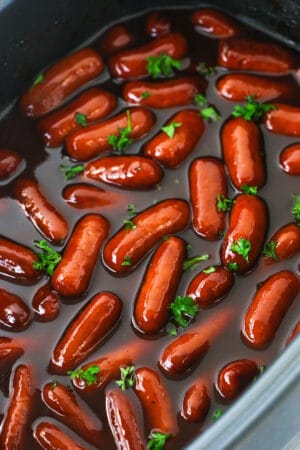 A Crockpot filled with cocktail weenies and a mixture of BBQ sauce and grape jelly