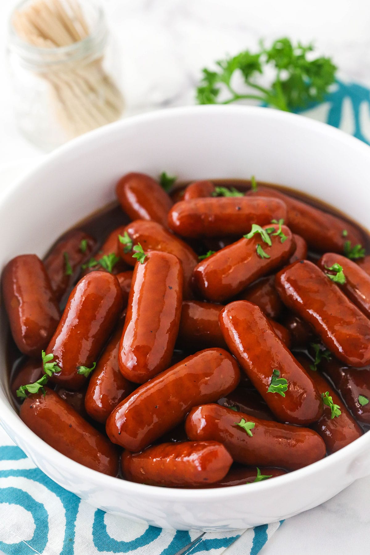 A bowl filled with grape jelly little smokies with a jar of toothpicks in the background