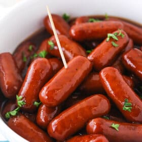 Grape jelly cocktail weenies in a large bowl with a toothpick sticking into one of them