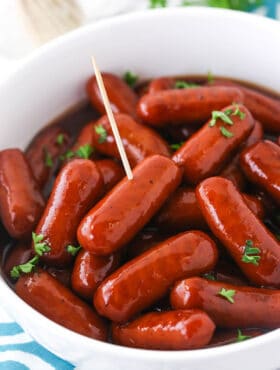 Grape jelly cocktail weenies in a large bowl with a toothpick sticking into one of them