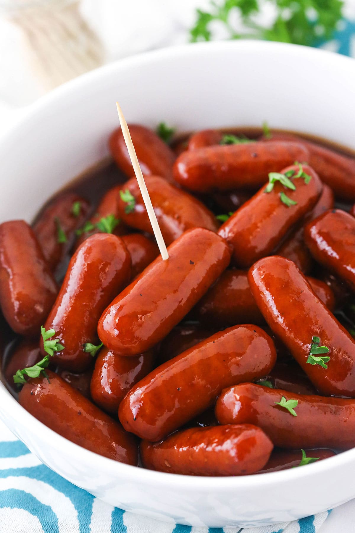 Grape jelly cocktail weenies in a large bowl with a toothpick sticking into one of them