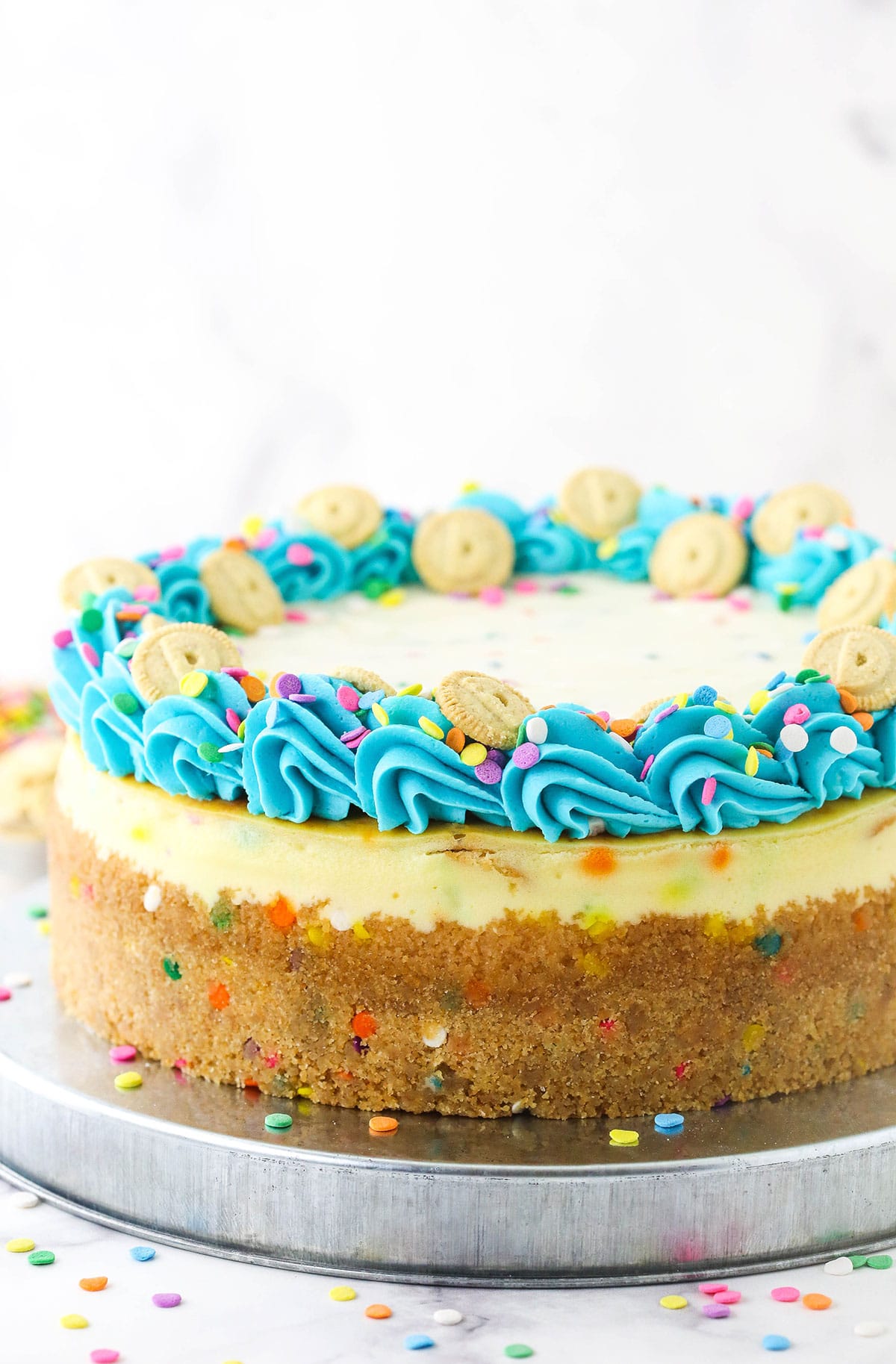 A Dunkaroo cookie cheesecake topped with rainbow chip frosting and a rim of bright blue buttercream