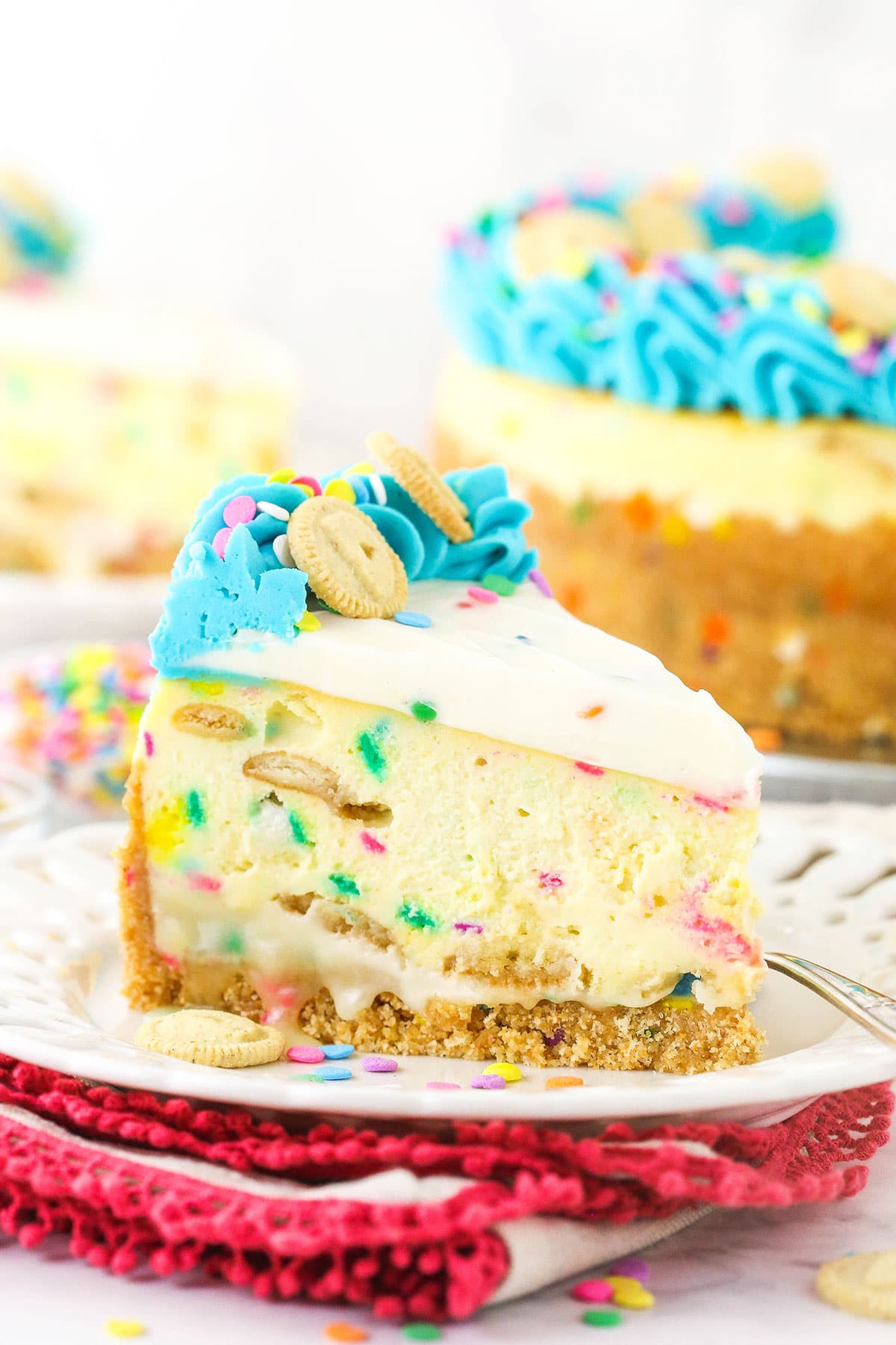 A piece of Dunkaroos cheesecake on a dessert plate with the remaining cake in the background