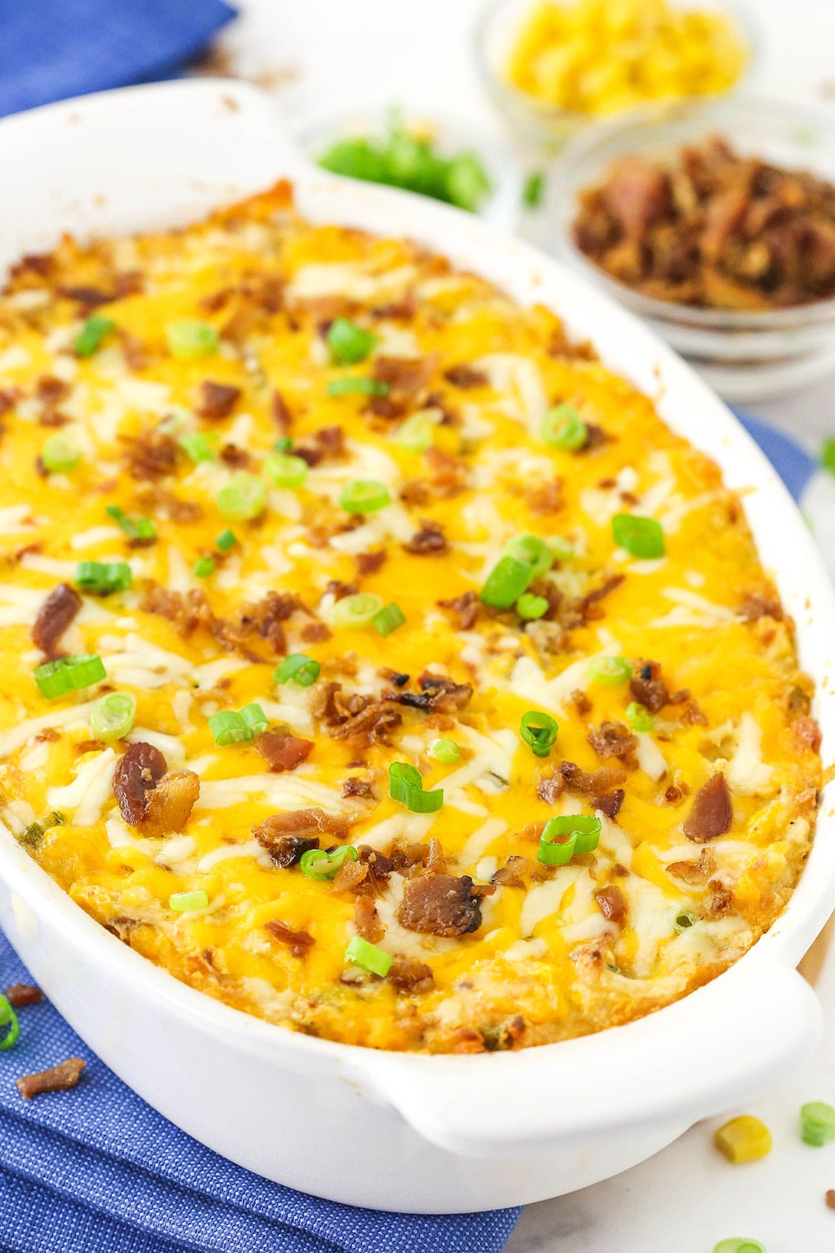 Hot corn and bacon dip inside of a baking dish on top of a blue kitchen towel