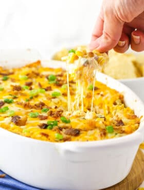 A chip that has just been dunked into a dish of corn dip and is being pulled out with gooey cheese sticking from the chip to the top of the dip
