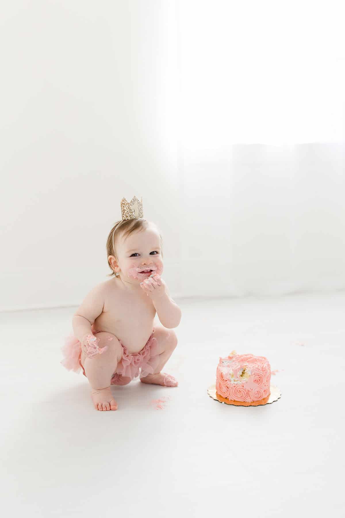 McKenzie kneeling by the smash cake and taking a bite