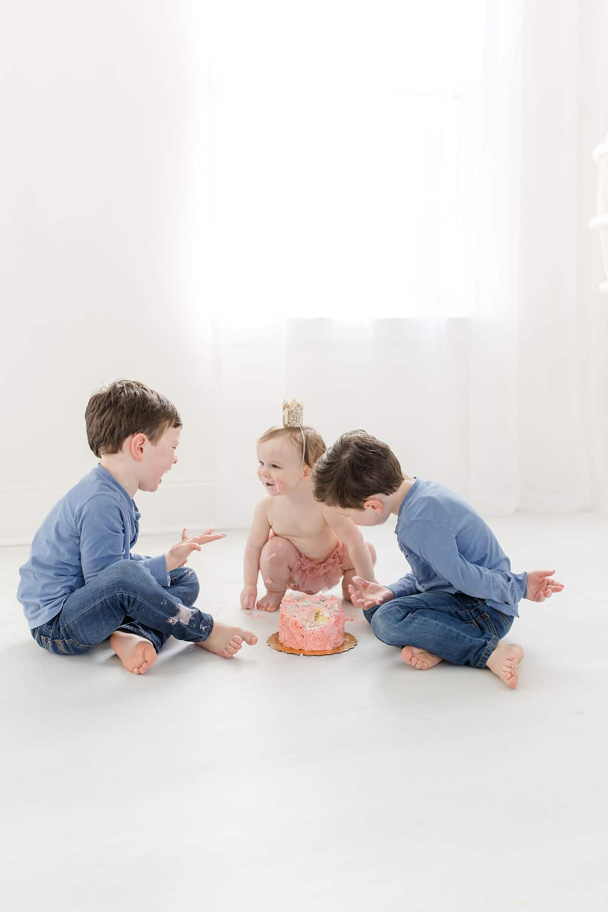 All three kids sitting around a smash cake and eating it