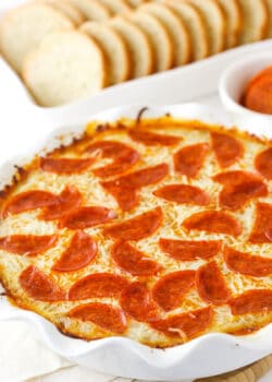 Pizza dip in a white dish, with a white dish of sliced French bread and a cup of marinara.
