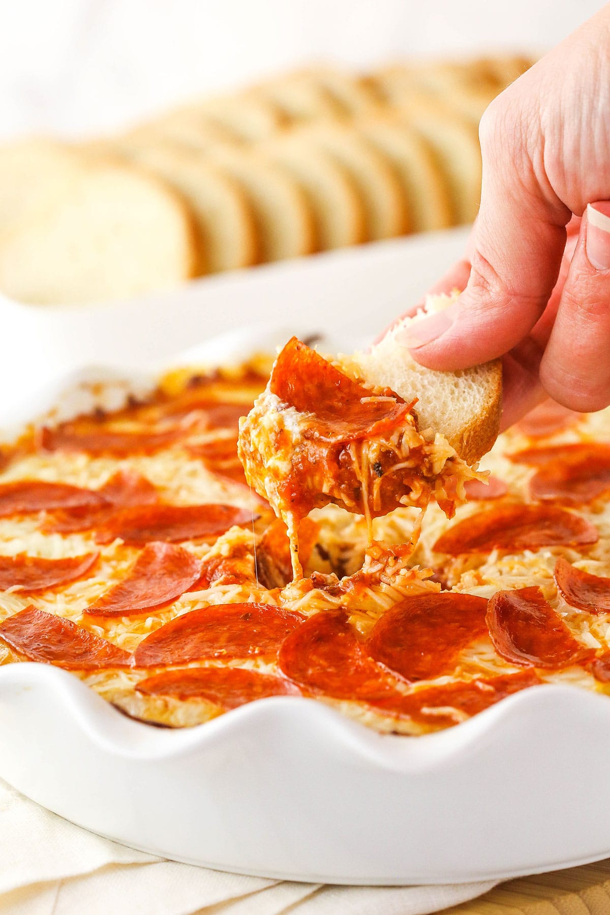 A woman's hand lifts dip from a dish with a small slice of French bread.