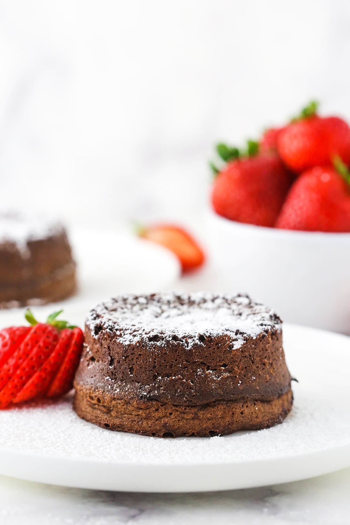 chocolate lava cake on white plate with sliced strawberry