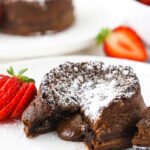 chocolate lava cake with lava center on white plate and sliced strawberry