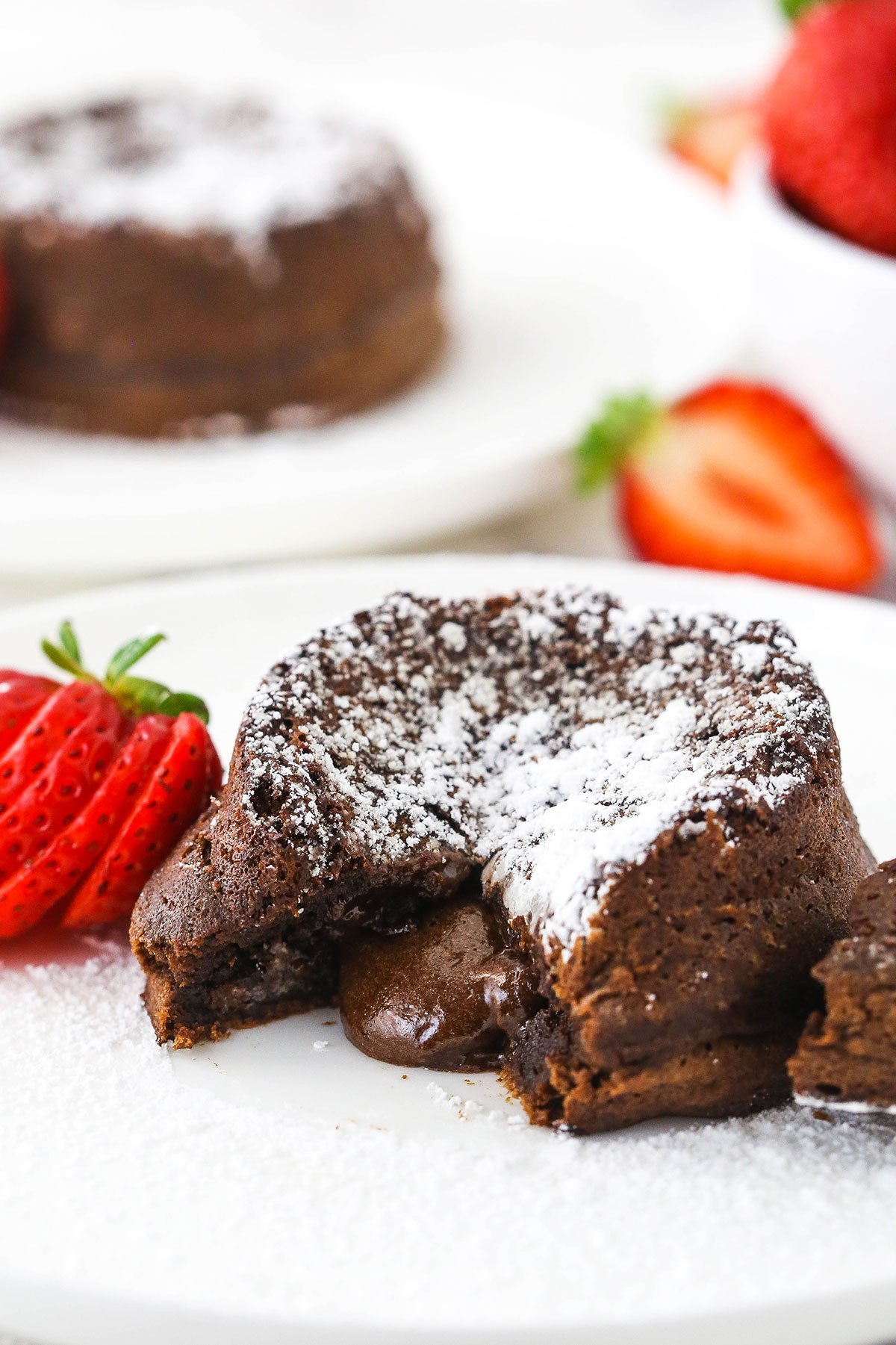 chocolate lava cake with lava center on white plate and sliced strawberry