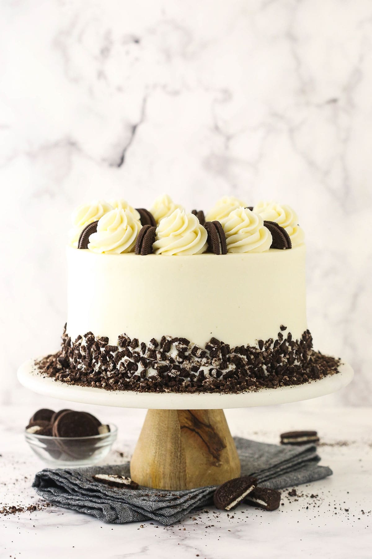 A smoothly frosted and beautifully decorated cookies and cream cake on top of a cake stand with Oreo cookies underneath it