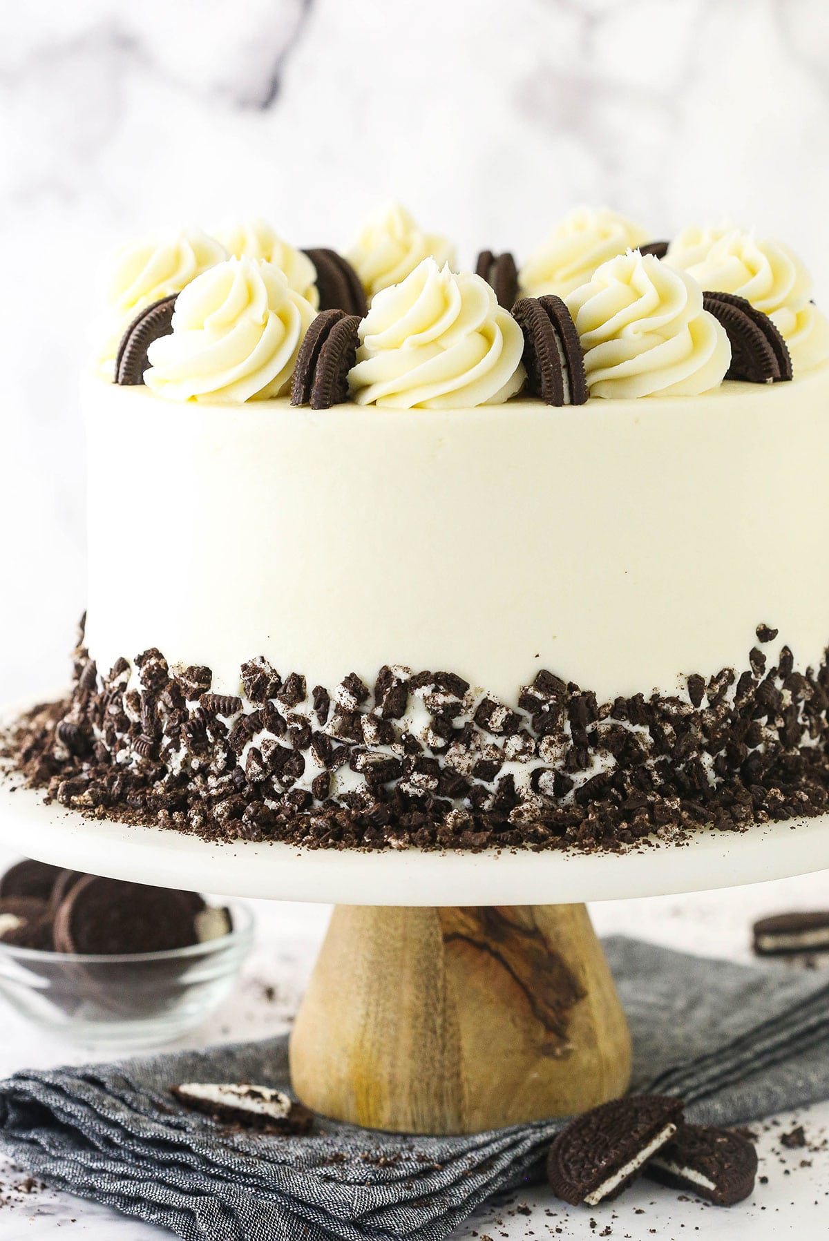 An Oreo layer cake on a wooden cake stand on top of a gray kitchen towel