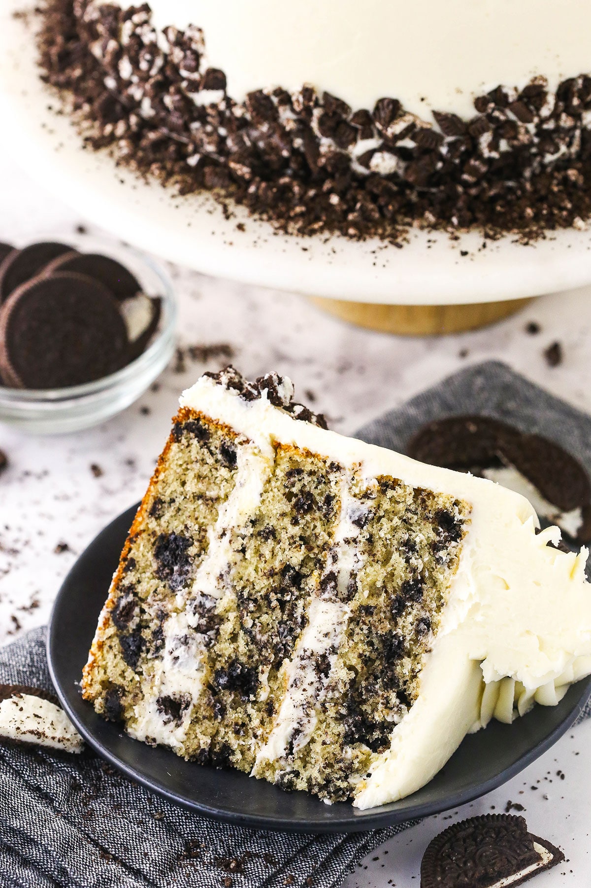 A large slice of cookies and cream layer cake on a black plate with the remaining cake behind it