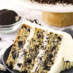 A piece of Oreo layer cake on a dessert plate with Oreo cookies and more cake in the background