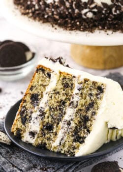 A piece of Oreo layer cake on a dessert plate with Oreo cookies and more cake in the background