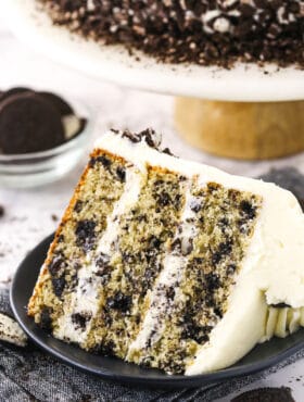 A piece of Oreo layer cake on a dessert plate with Oreo cookies and more cake in the background