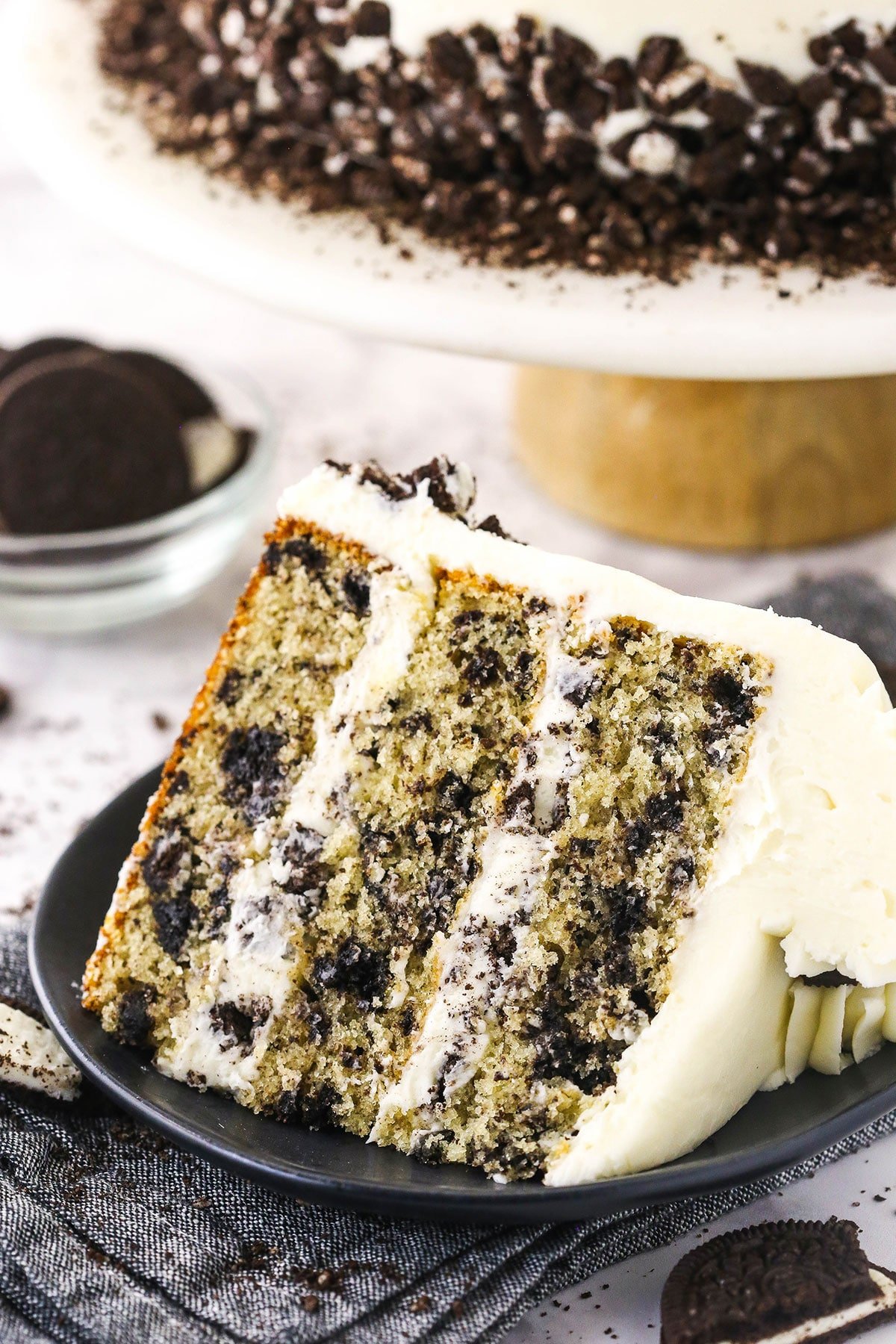 A piece of Oreo layer cake on a dessert plate with Oreo cookies and more cake in the background