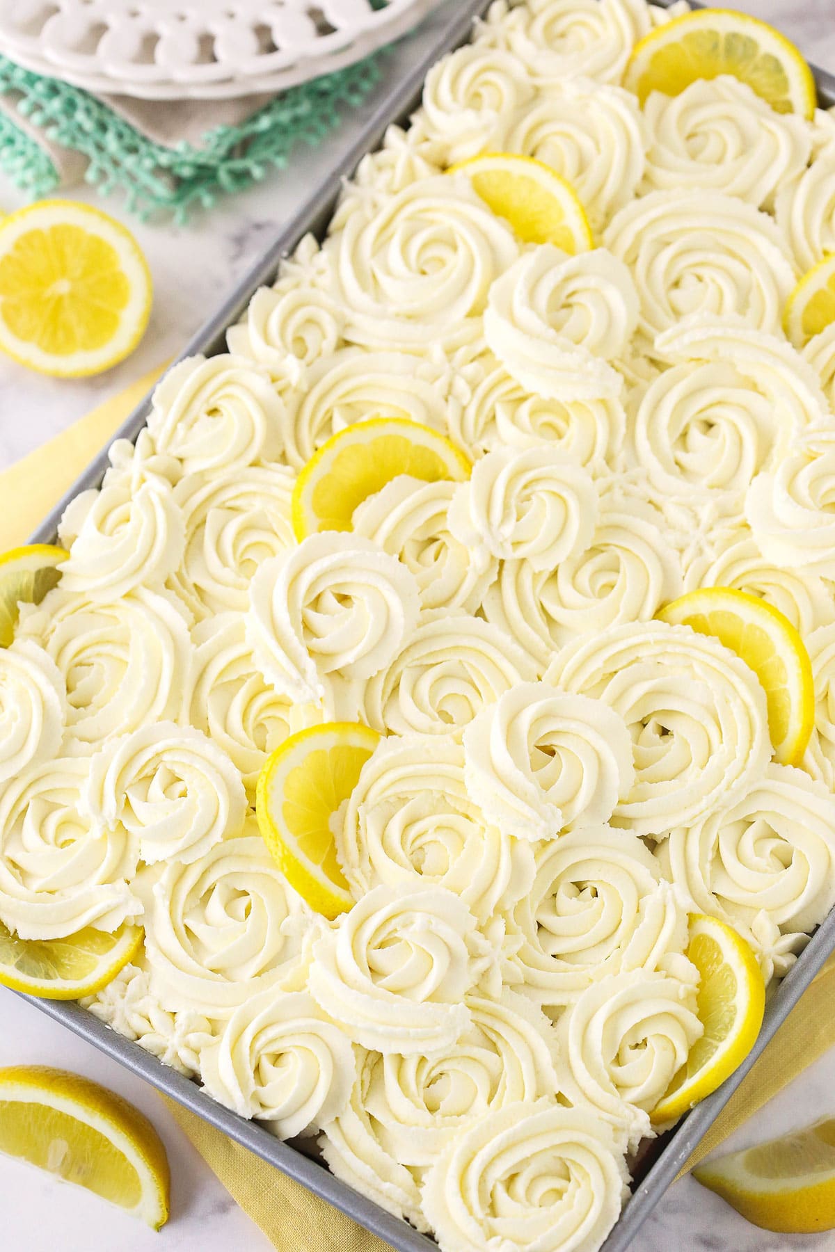 A lemon poke cake inside of a 9x13-inch pan with mascarpone whipped cream frosting piped on top of it