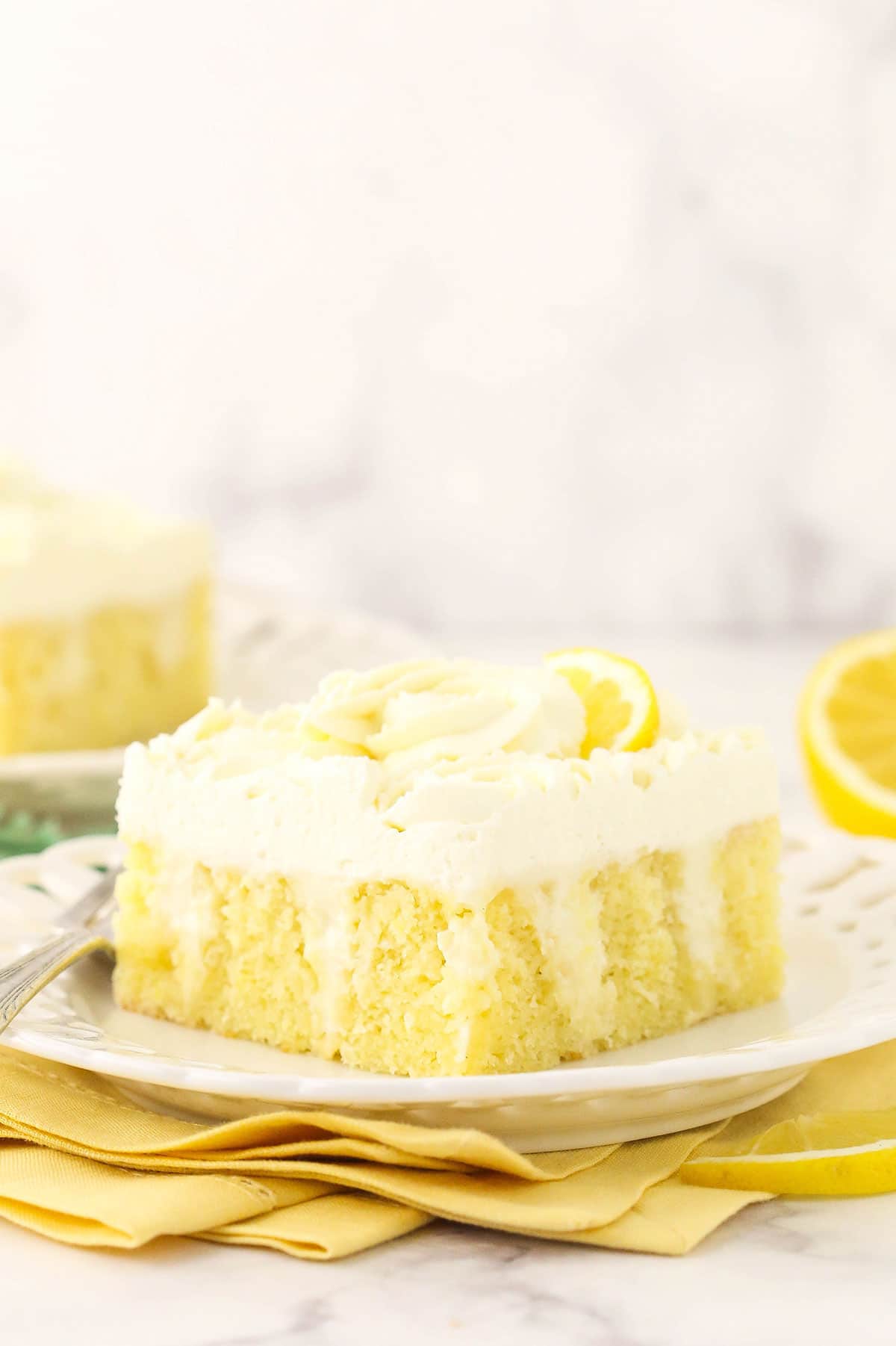 A slice of lemon poke cake on a white plate on top of a marble countertop