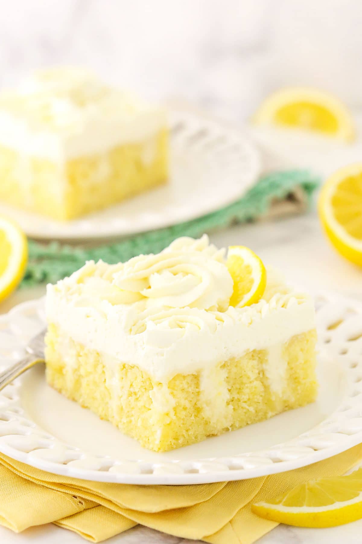 A piece of lemon poke cake on a plate with folded up cloth napkins underneath it