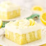 A slice of lemon poke cake on a dessert plate with another piece on a plate in the background