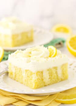 A slice of lemon poke cake on a dessert plate with another piece on a plate in the background