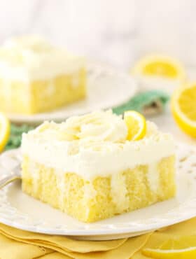 A slice of lemon poke cake on a dessert plate with another piece on a plate in the background