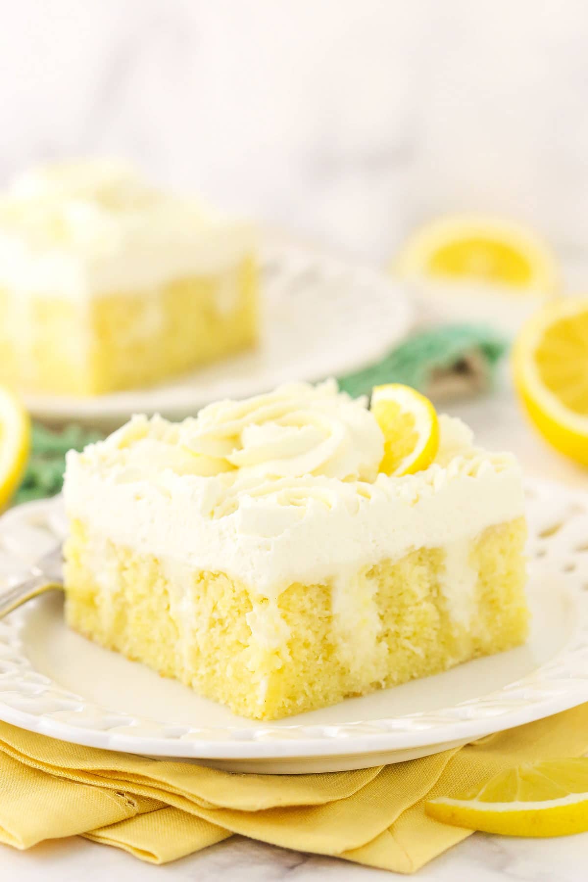 A slice of lemon poke cake on a dessert plate with another piece on a plate in the background