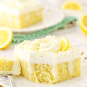 A piece of lemon poke cake on a plate with one bite on a metal fork