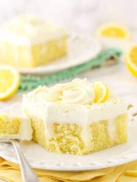 A piece of lemon poke cake on a plate with one bite on a metal fork