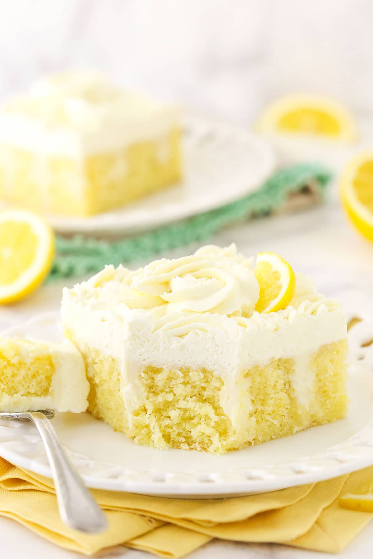 A piece of lemon poke cake on a plate with one bite on a metal fork