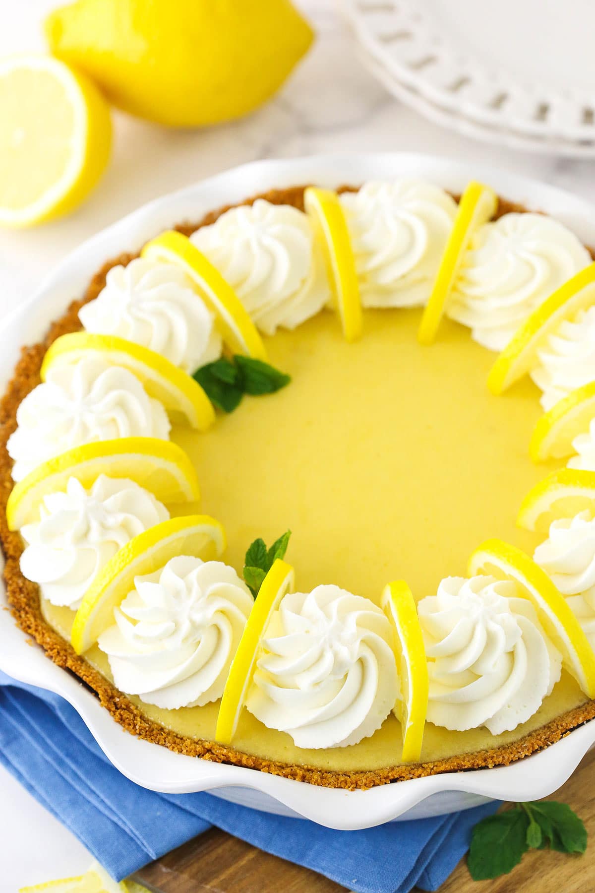 A creamy lemon pie topped with swirls of homemade whipped cream, fresh lemon slices and a couple of mint leaves
